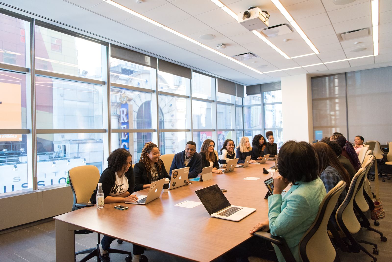 People around a conference table in a real meeting, laptops open.
